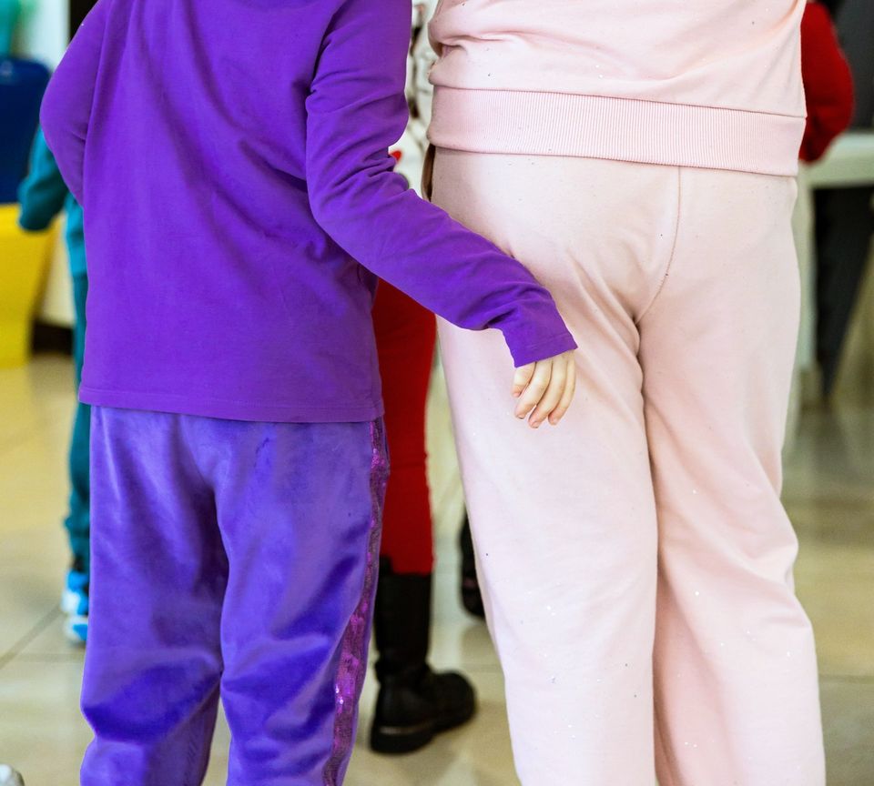 Due bambini di spalle, uno vestito di viola con il braccio intorno alla vita dell'altro, vestito di rosa