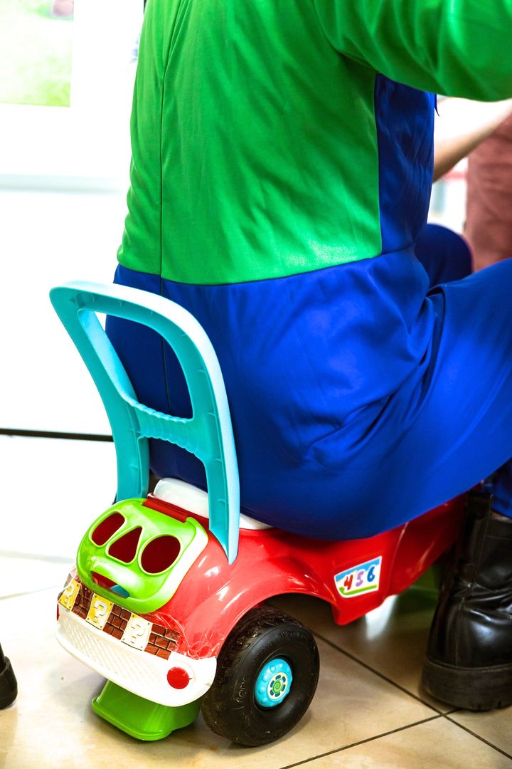 Un animatore in costume verde e blu a cavalcioni di una macchinina giocattolo