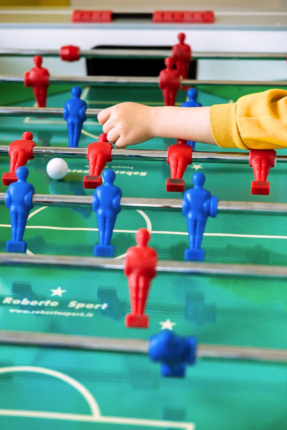 Una mano di bambino sul campo di un calcio balilla, fra gli omini rossi e blu