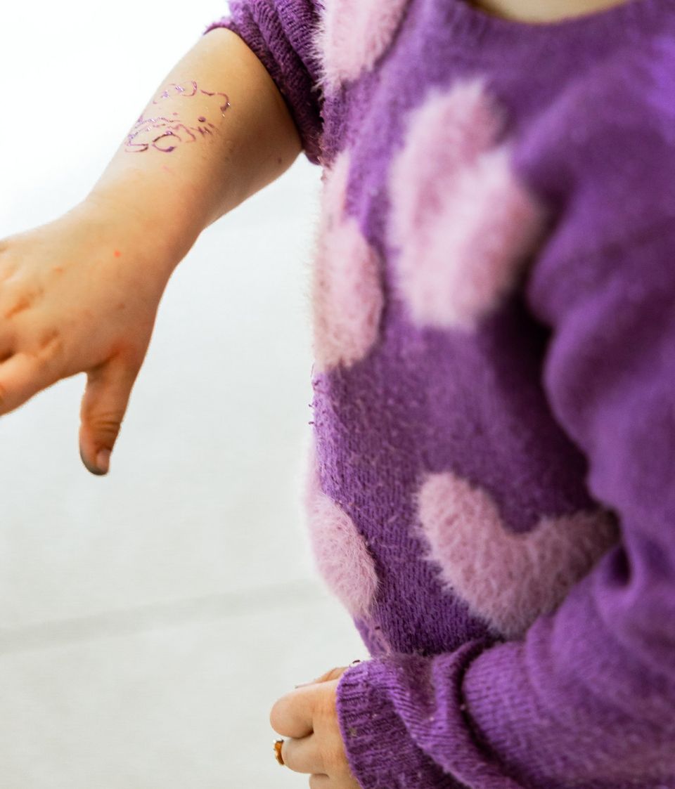 Un braccio con un tatuaggio finto appena fatto, accanto a un maglione viola a cuori