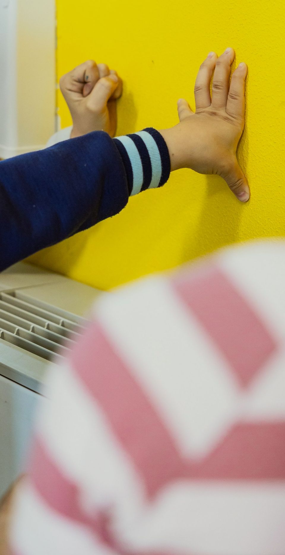 Due mani di bambino appoggiate a una parete gialla durante un gioco
